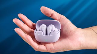 the jlab go pods anc earbuds in lilac with a lilac charging case and built in usb-c cable against a blue background on a marble stand