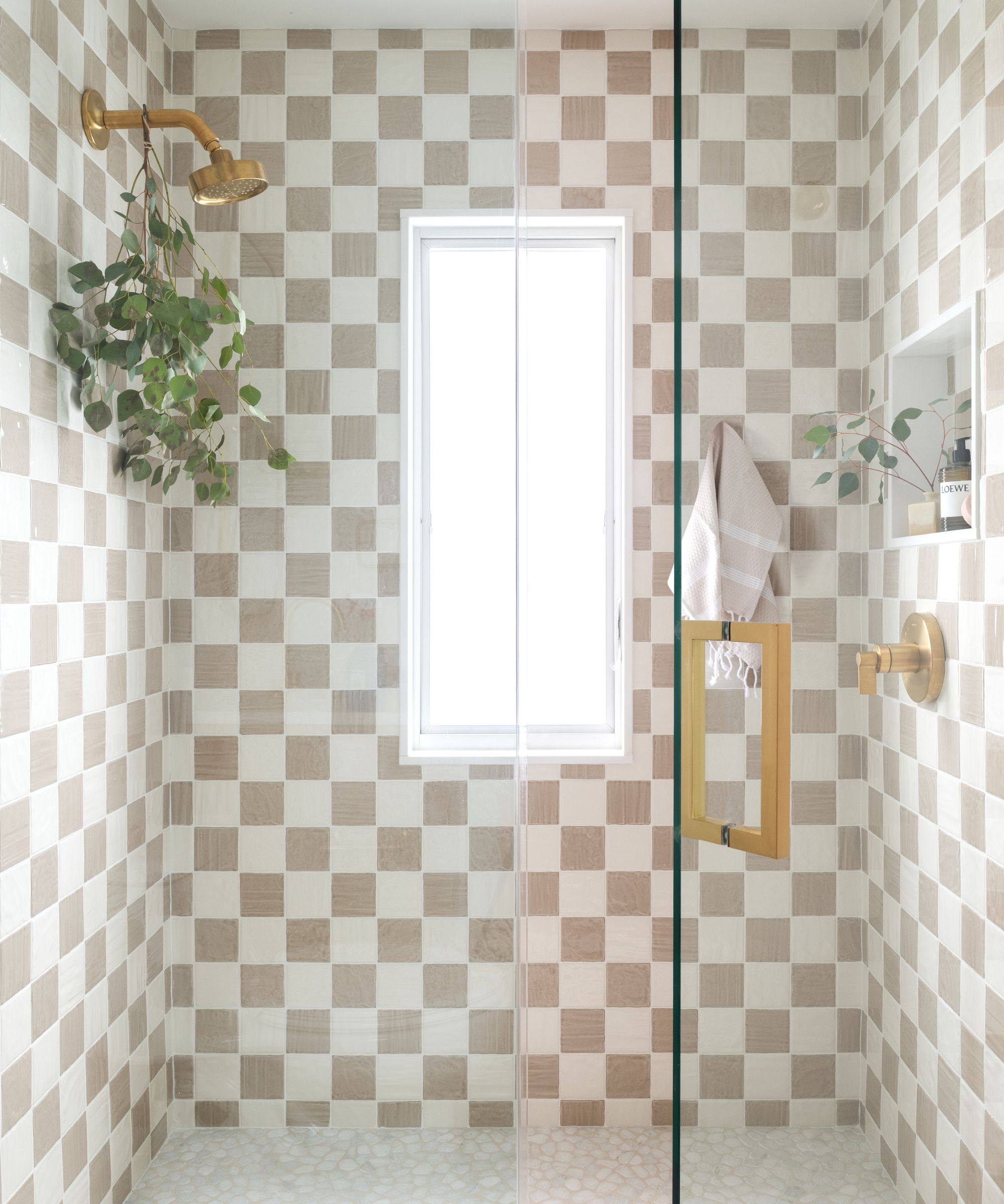 A shower with white and beige checkerboard tiles and gold hardware