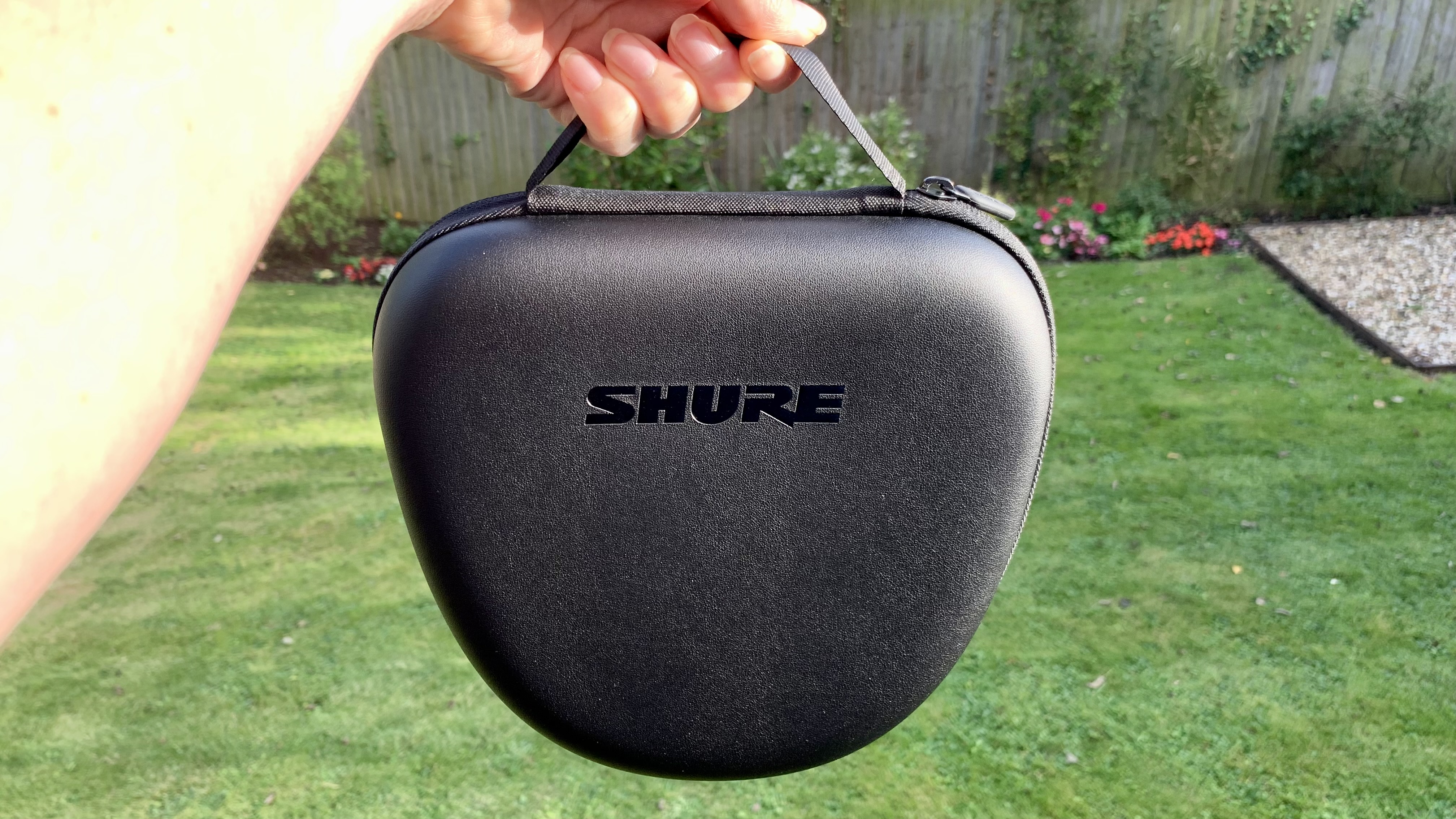 Shure Aonic 50 Gen 2 case, held in hand with a garden in the background