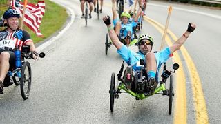 A male hand cyclist in a blue tshirt rides downhill with his arms aloft