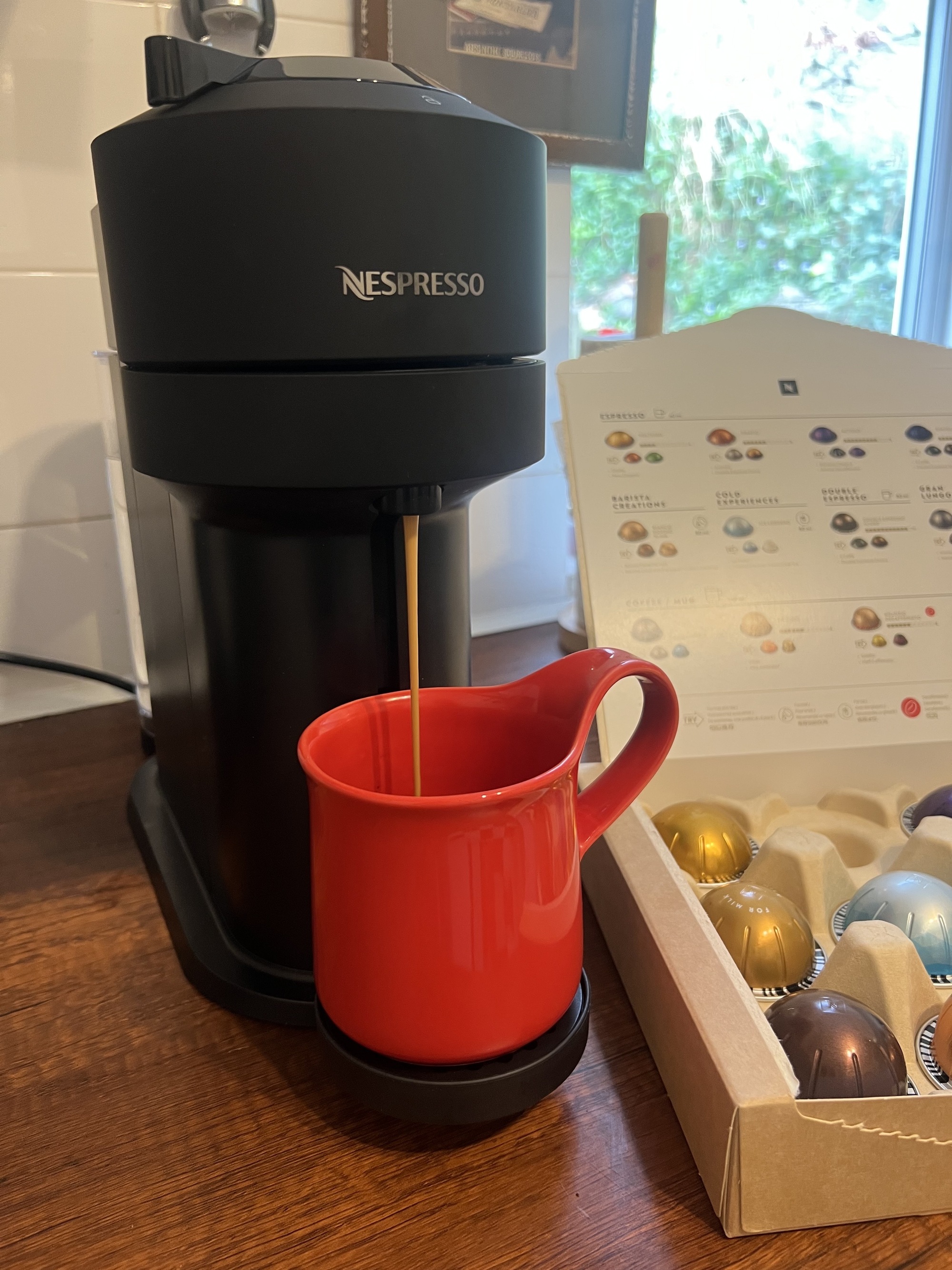 Image of a red coffee mug on a black Nespresso Vertuo Next machine with an espresso shot brewing into it.