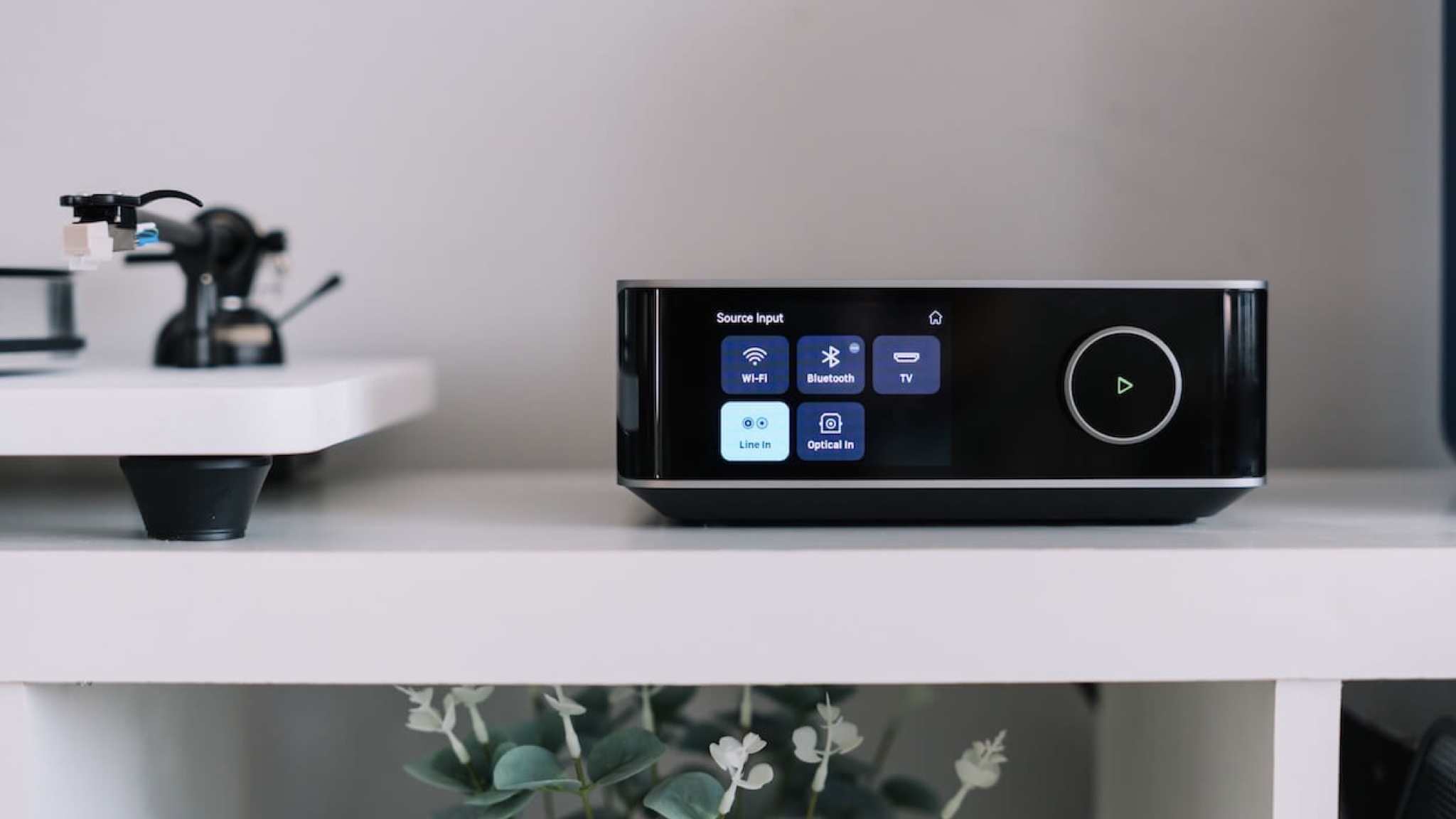 A lifestyle photo of the WiiM Amp Ultra on top of a white unit with a white and black turntable beside it