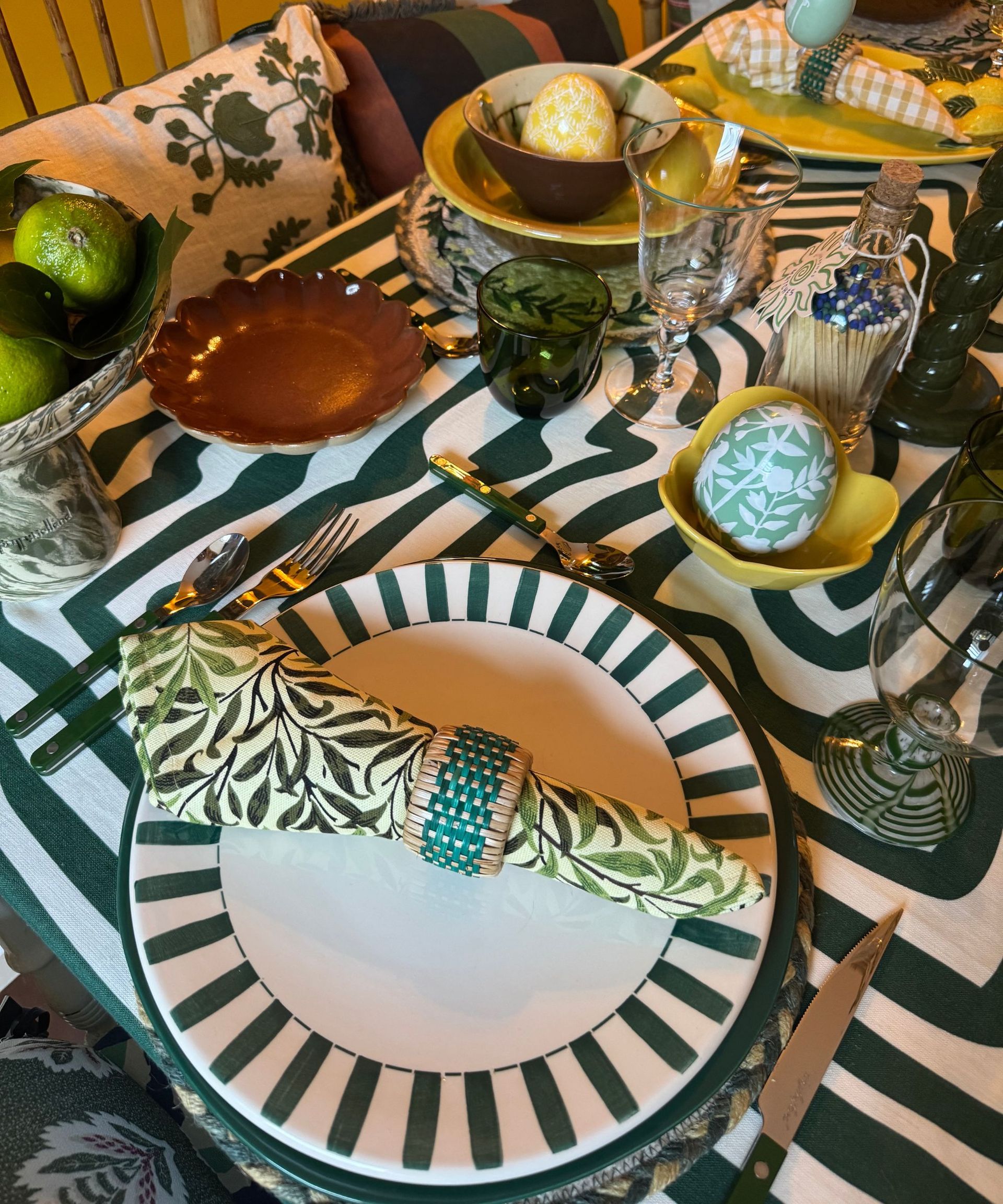 Green, white and yellow themed table setting with a striped tablecloth, mis-matched plates and napkins and Easter egg ornaments