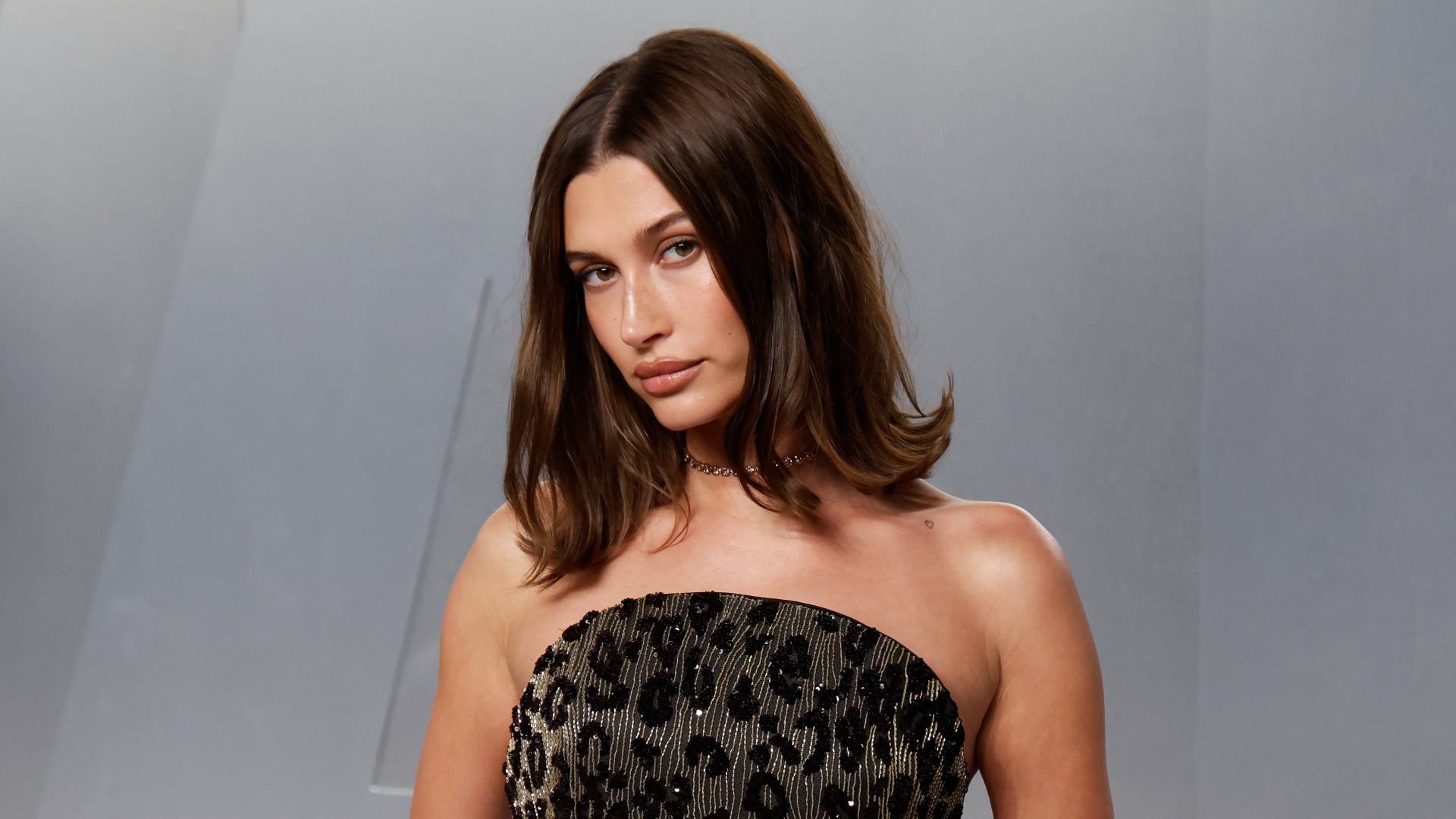 a white woman with short hair poses at a red carpet event in front of a gray background