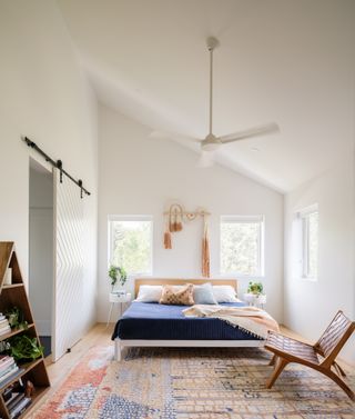 White bedroom with multicolored flatweave rug, wooden bed and dark blue duvet cover