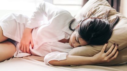 Woman Touching Abdomen In Pain While Sleeping On Bed At Home - stock photo