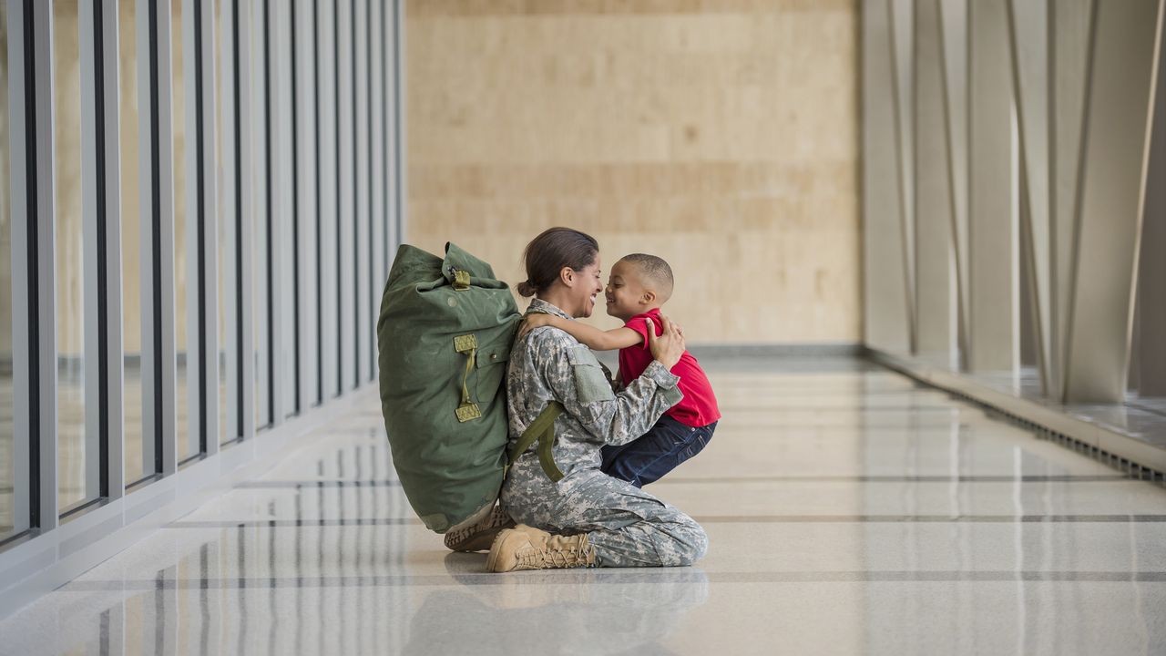 A young woman in a military uniform embraces a young child in a corridor.