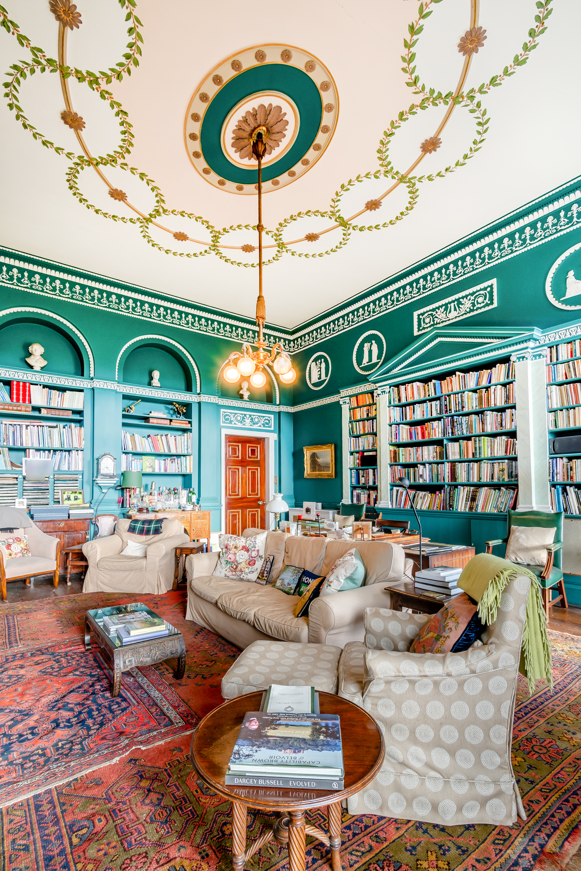 A library with sofas, teal walls and ornate ceiling detailing