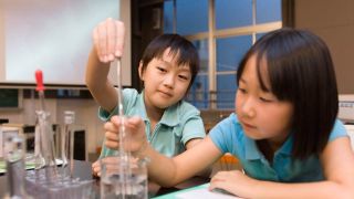 Two kids work with clear liquid in a beaker