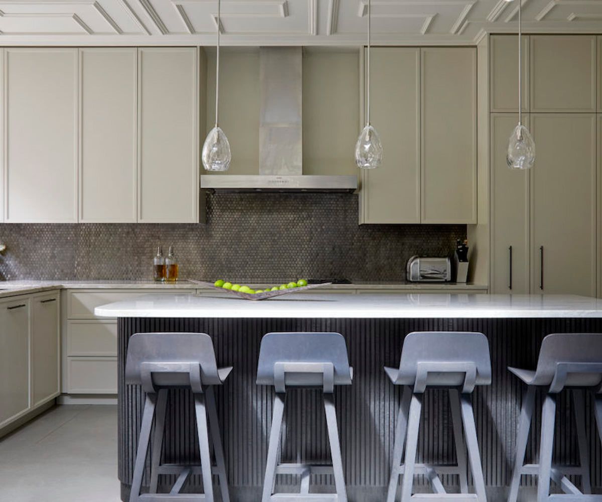 A kitchen island with overhead lights and beige kitchen cupboards