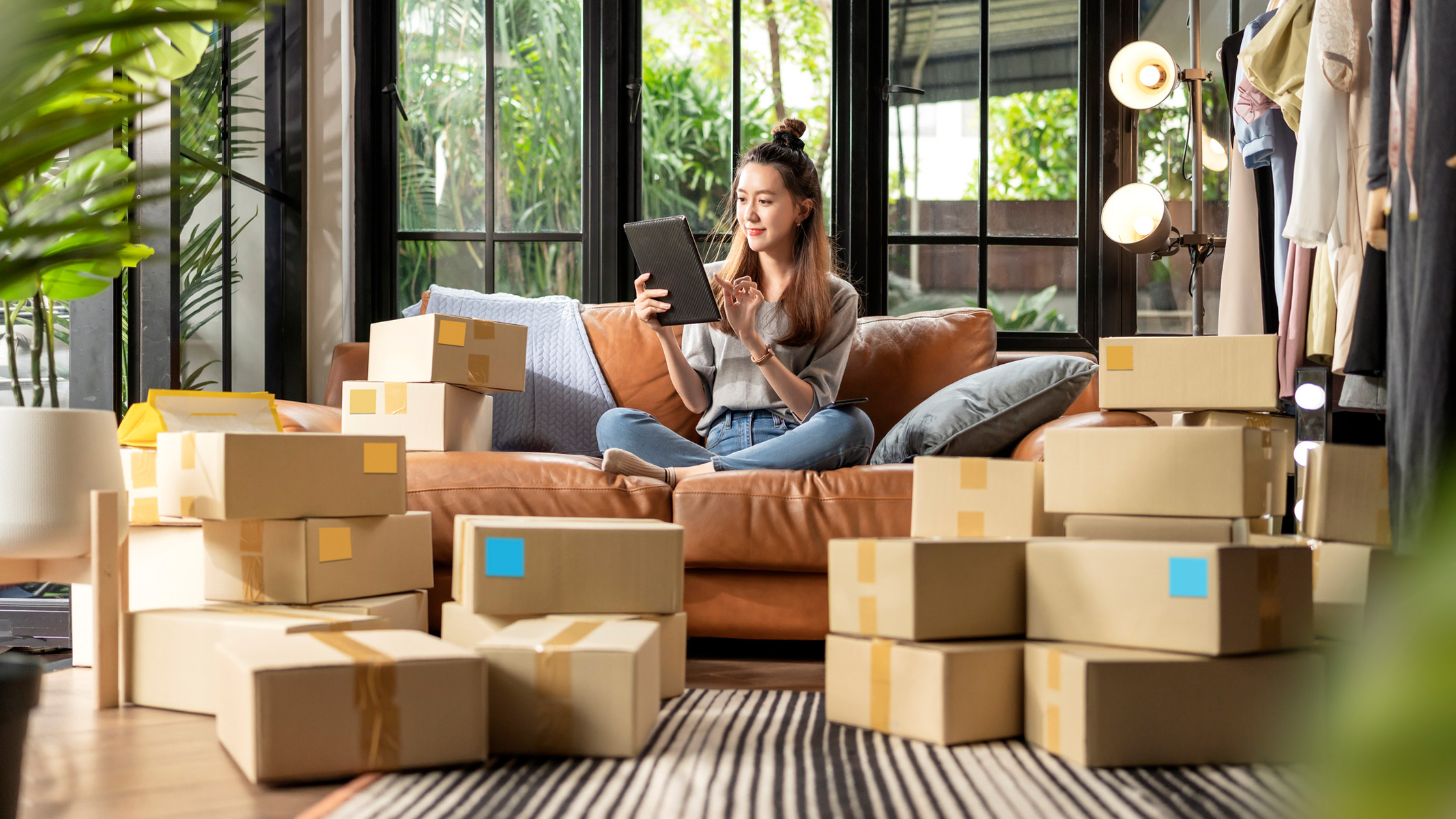 woman sat on a sofa with a tablet among lots of brown boxes