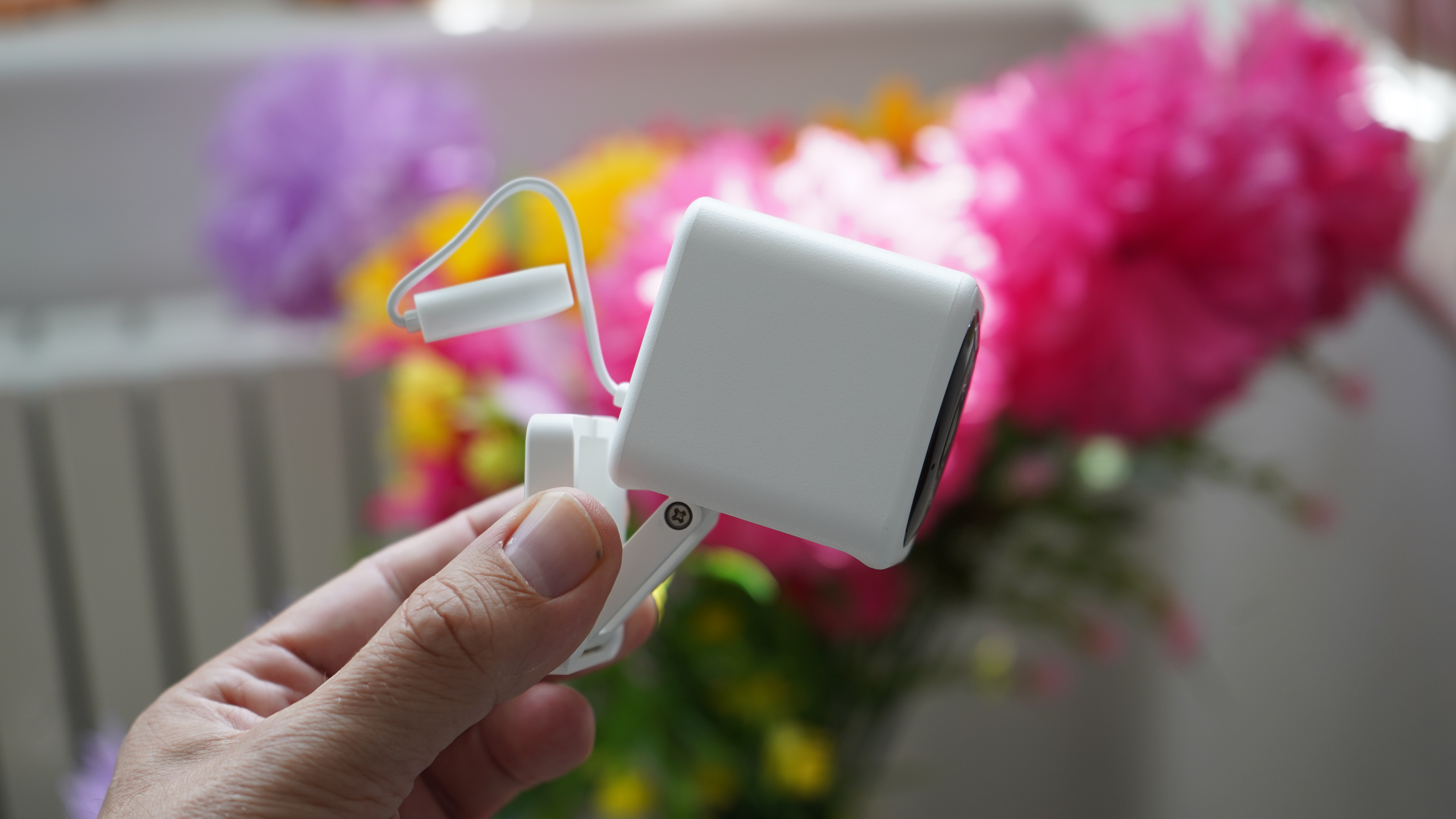 Wyze Cam v4 seen from the side held in hand with flowers behind