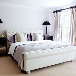 bedroom with white wall and bedside table and lamp and white window with curtains