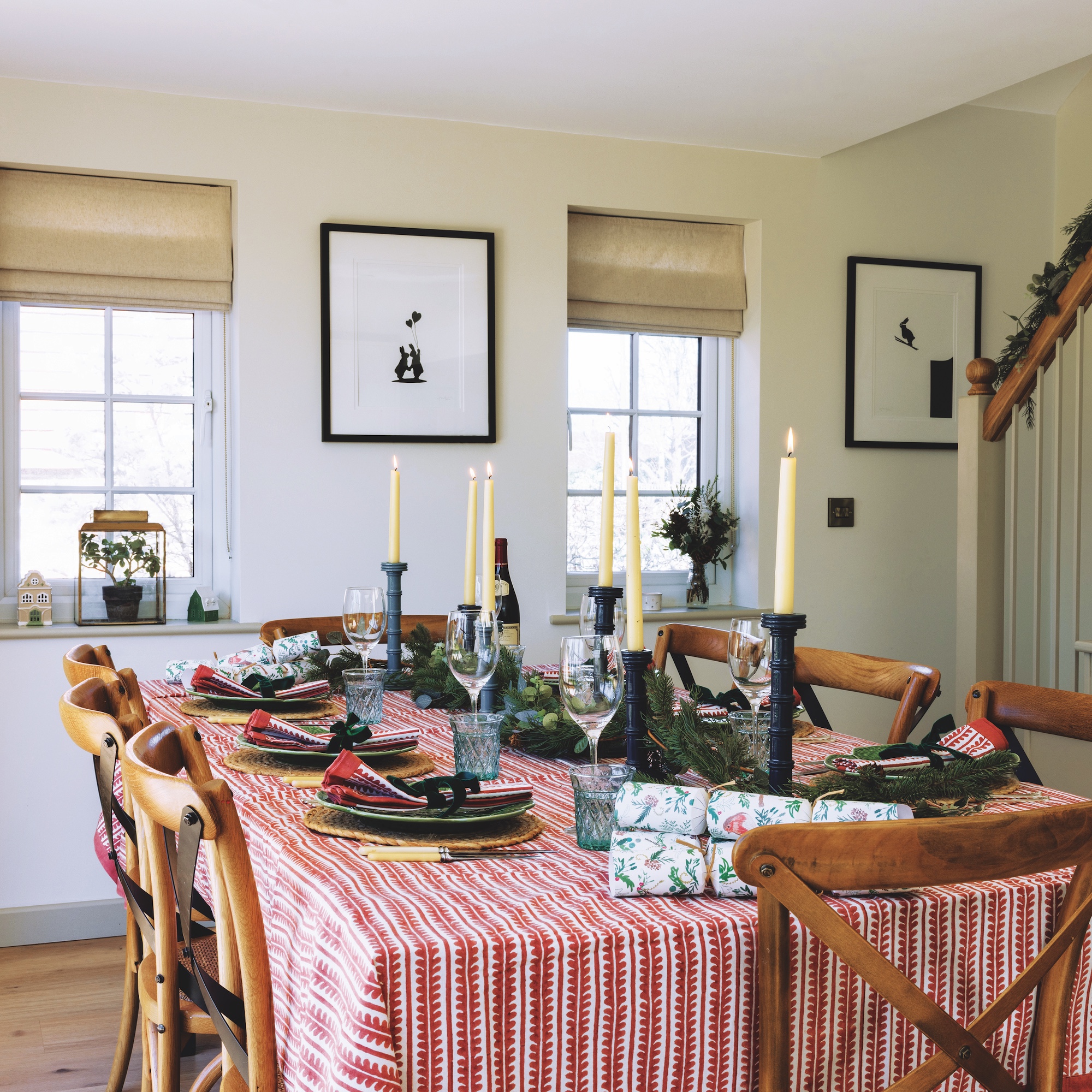 dining room with table covered in red and white stripe cloth, wooden dining chairs, black candlesticks and white walls