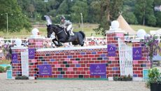 A black horse clears a big red puissance wall at Bolesworth International horse show
