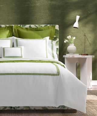 Matouk Schumacher Sheet Set on a bed against a green wall with a white nightstand to the right.