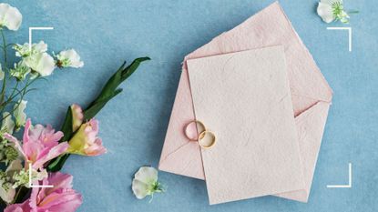 A blank piece of paper sits on an open pink envelope and blue background while someone considers what to write in a wedding card