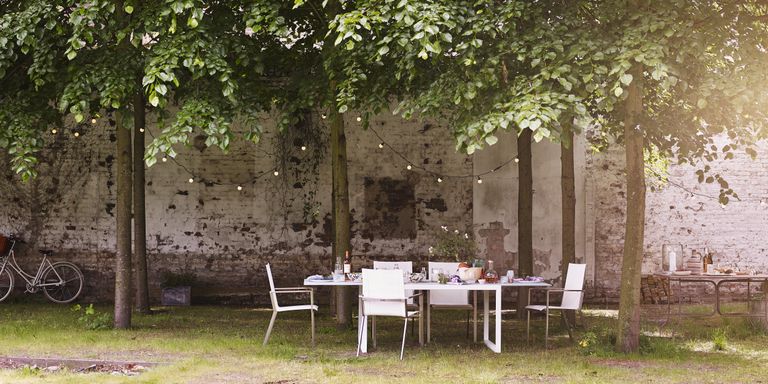 园林隐私想法，包括砖墙，砖墙，串灯和白色的桌子和椅子。