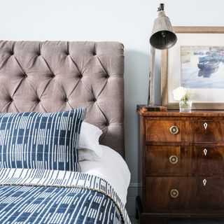 bedroom with small chest of drawers for bedside table and pair with a linen button back headboard and printed bedding