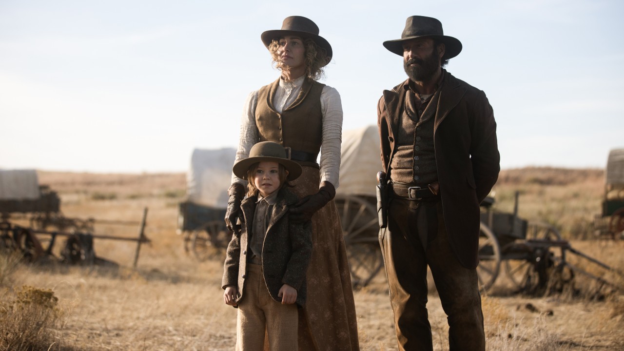 Faith Hill, Tim McGraw and Audie Rick standing in front of a bunch of wagons.