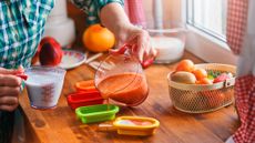 Person pouring blended fruit out of a glass jug into a ice lolly mold