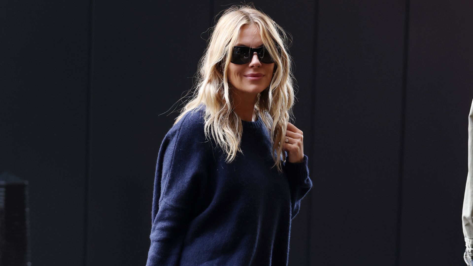 Sienna Miller steps out in London wearing flat black knee-high boots from Dune. She styled them with a grey knit and black knee-length shorts.