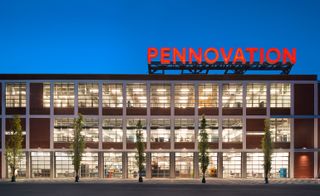Lit, red brick building at night, with the bright red "Pennovation" sign contrasting the deep blue sky