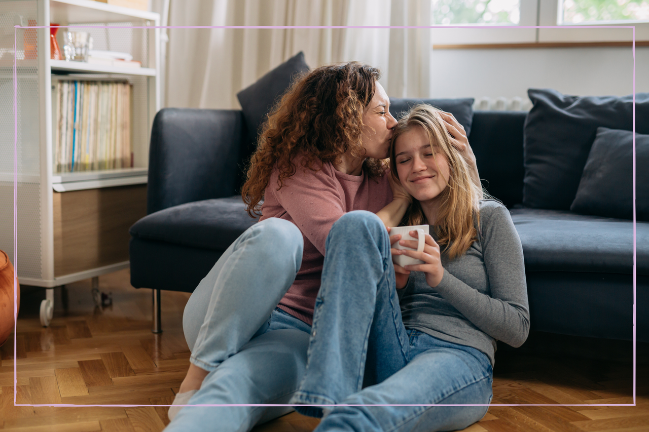 Mother kisses her daughter while sitting on floor in living room