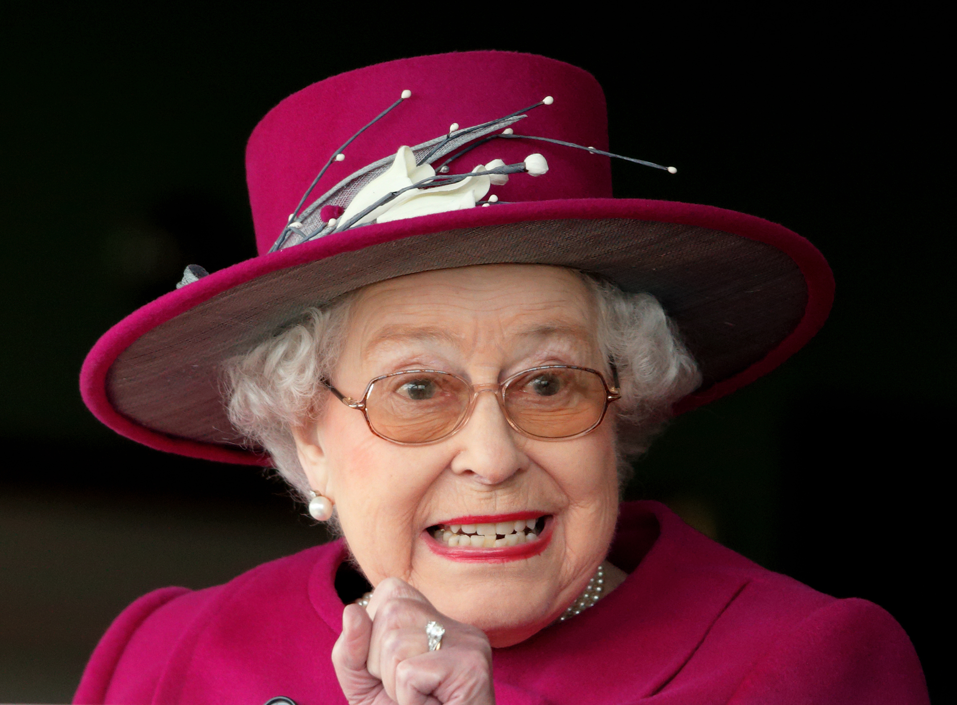 Queen Elizabeth wearing a berry hat and coat and grimacing