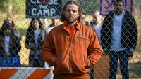 Max Thieriot as Bode standing with his hands in his pockets by in front of a gate.
