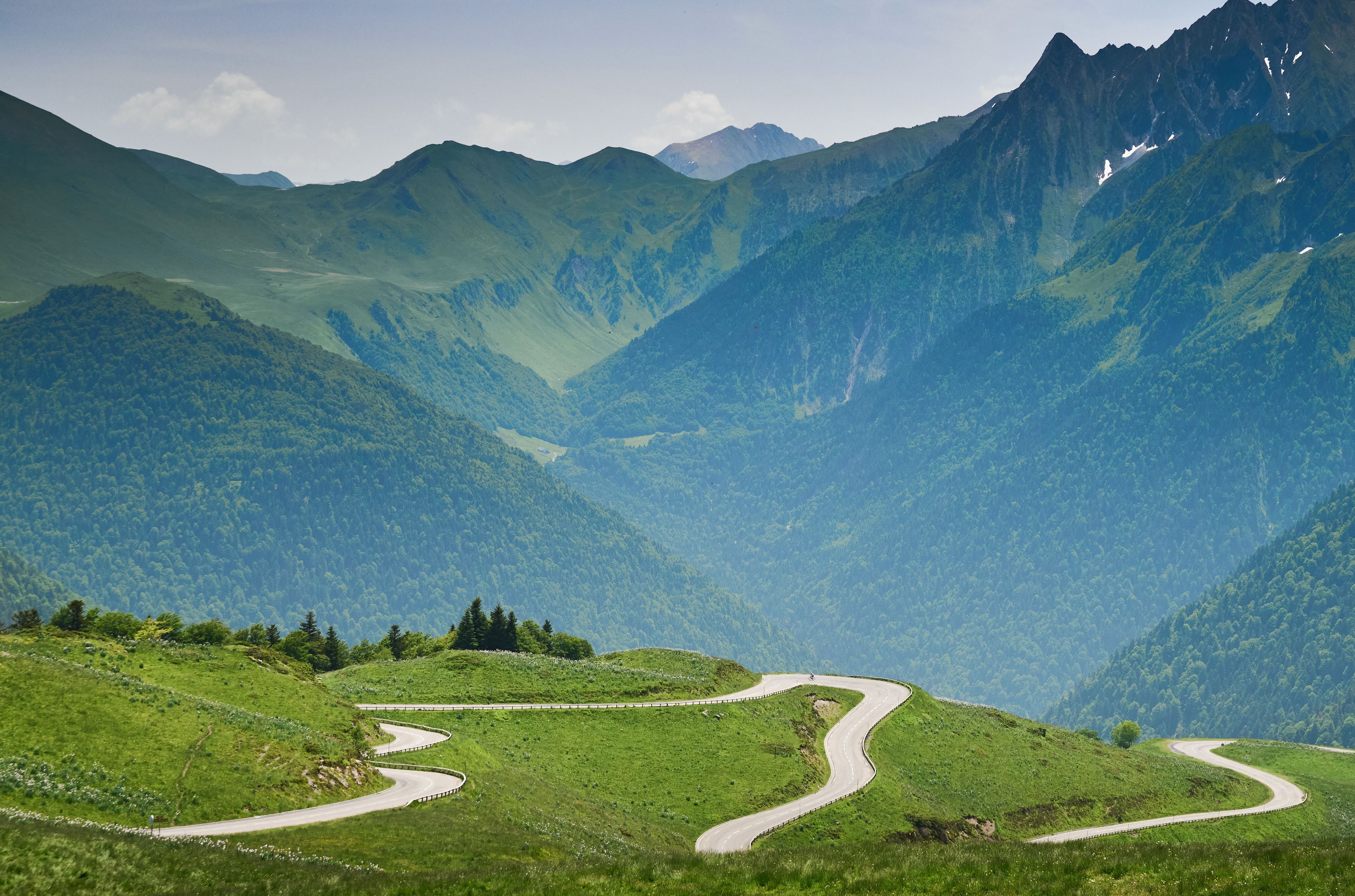 A winding road through lush green mountains, reminiscent of the scenic routes featured in cycling events like the Tour de France.