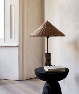 Rattan table light with marble base on black side table with pale plaster effect walls