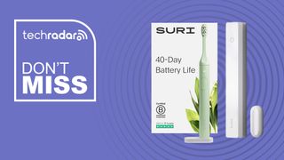 A green Suri Electric Toothbrush sits on its stand in front of its cleaning storage case.