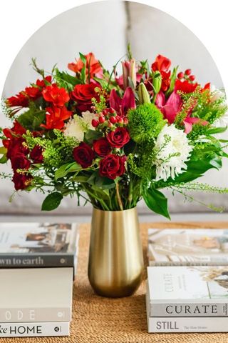 A bouquet of red flowers with some white and green foliage in a gold vase.