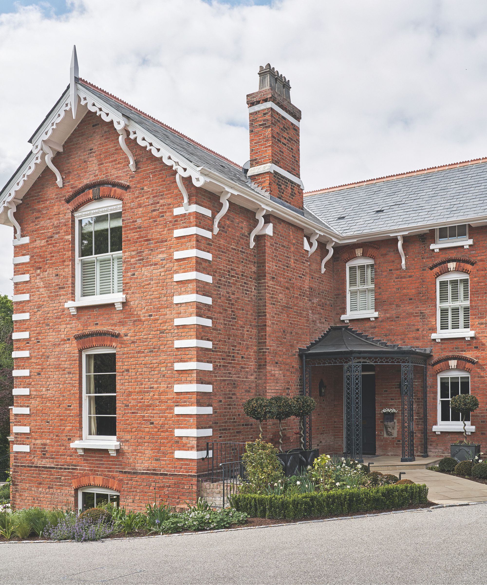 A large red brick house with a black awning over the front door and neat front garden with flowers and low hedging.