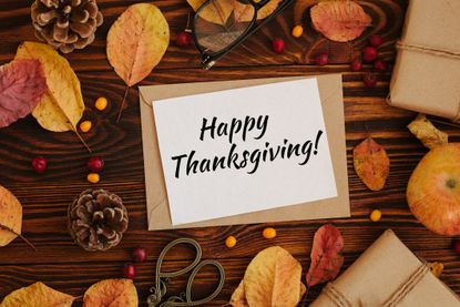 Happy Thanksgiving greeting card on wood table with leaves and pine cones