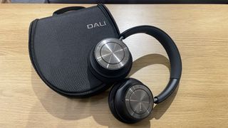 Dali IO-8 wireless over-ear headphones on top of case on wooden shelf