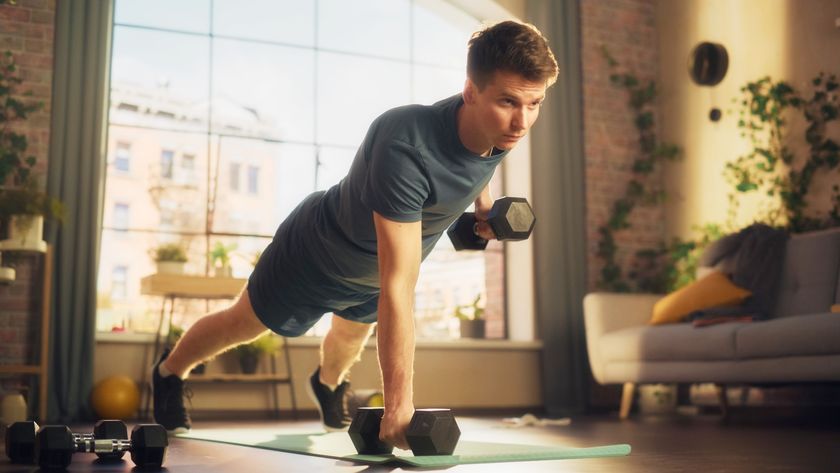 Man in home on an exercise mat performing a dumbbell renegade row with left arm lifted in row position from plank