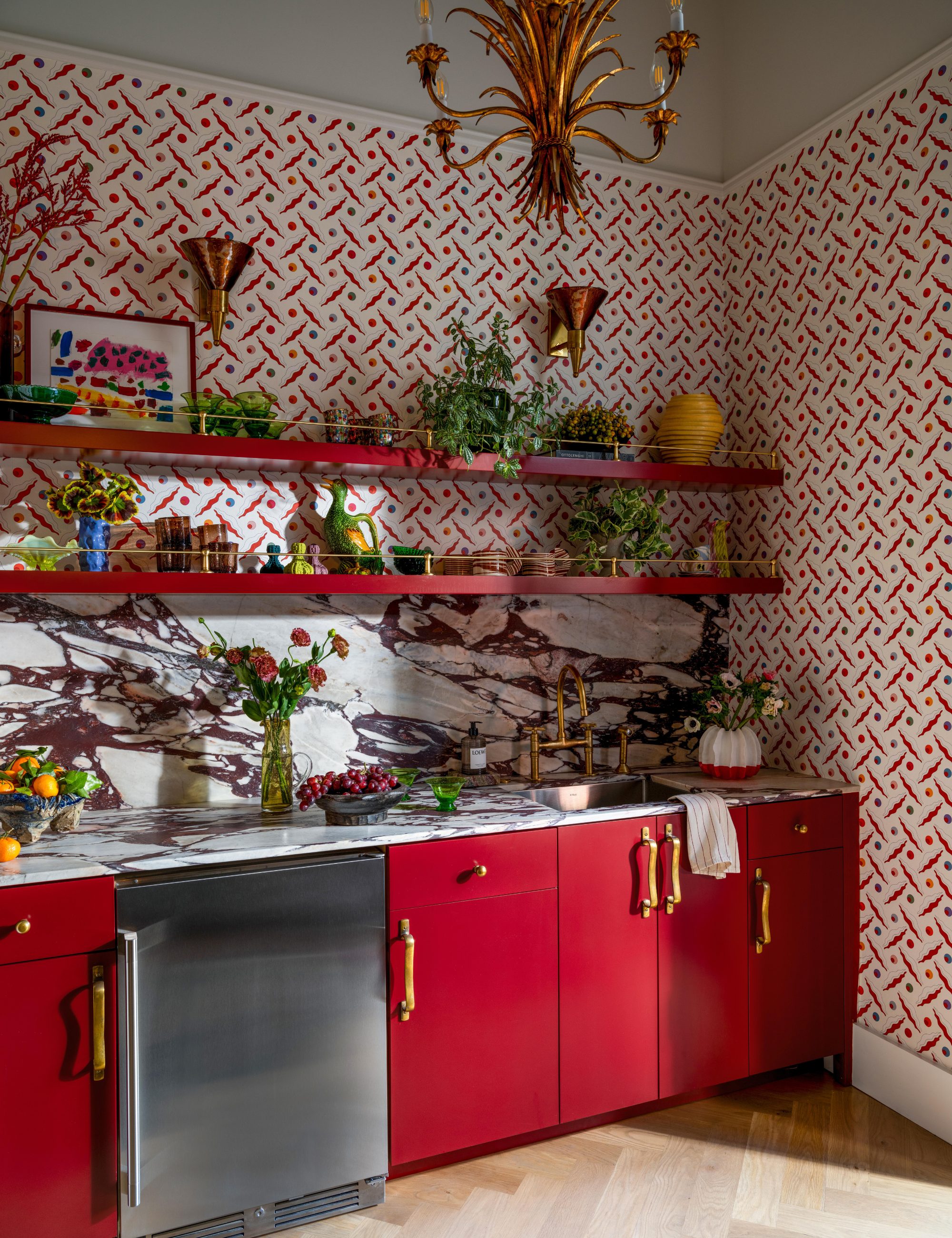 Bold kitchen featuring red cabinetry, a red-and-white marble backsplash, and red, cream, and blue geometric wallpaper