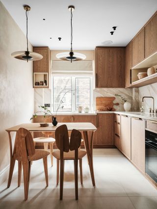 A modern neutral Scandinavian-inspired kitchen with wooden cupboards, feature chairs and hanging pendant lights