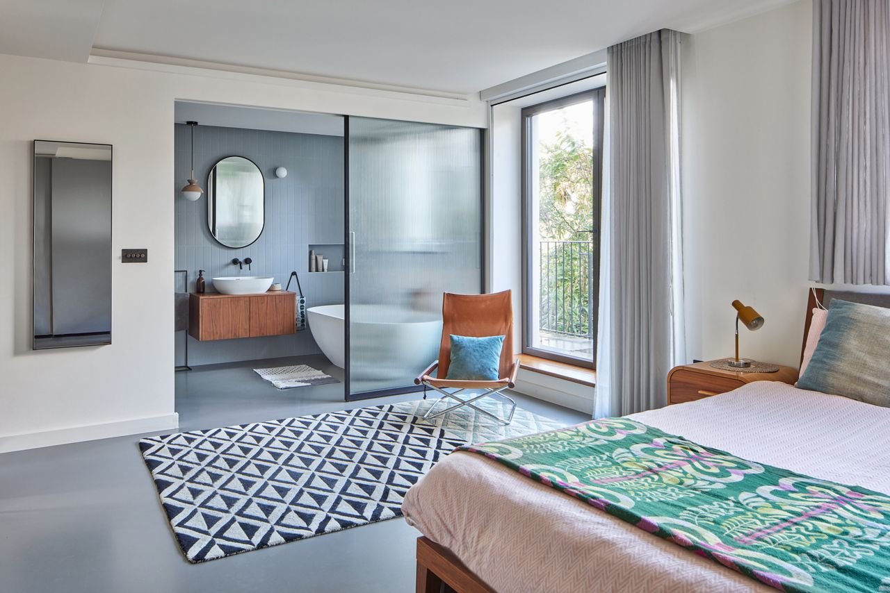 A bedroom with a large geometric rug leading to an ensuite bathroom with ribbed glass walls