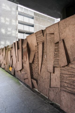 A photo of a concrete mural. Advancing and receding concrete planes make out the text.