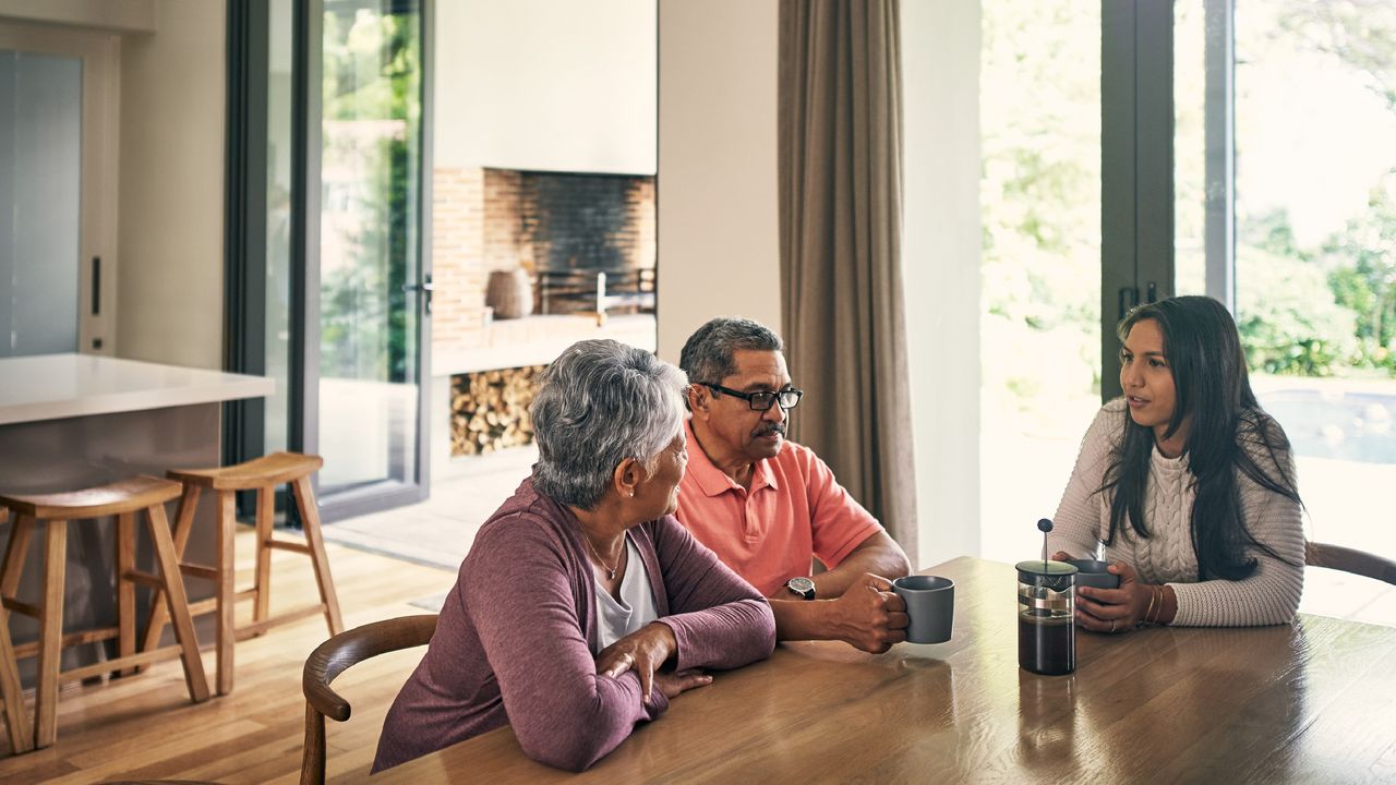 An older couple sit at the dining room table and talk seriously with their adult daughter.