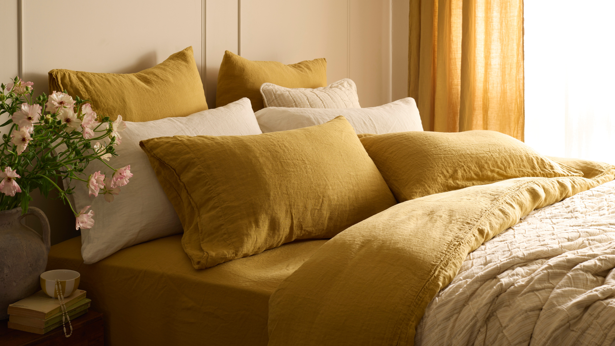 bedroom with mustard and cream sheets and flowers on bedside table