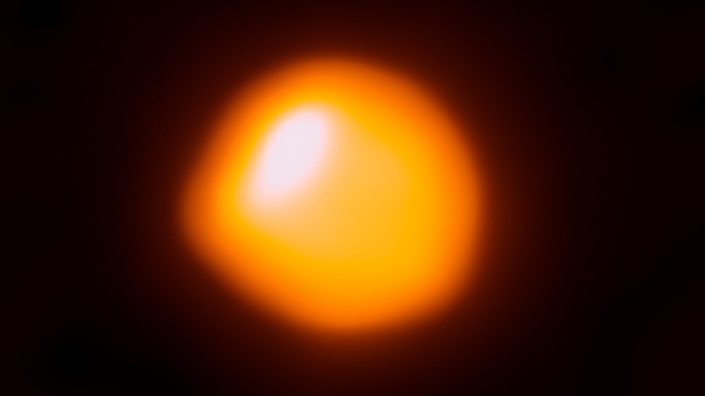 Betelgeuse star appearing as a bright orange orb with a darker orange outer rim and a white oval-shape glow in the top left portion of the star as viewed by ALMA.