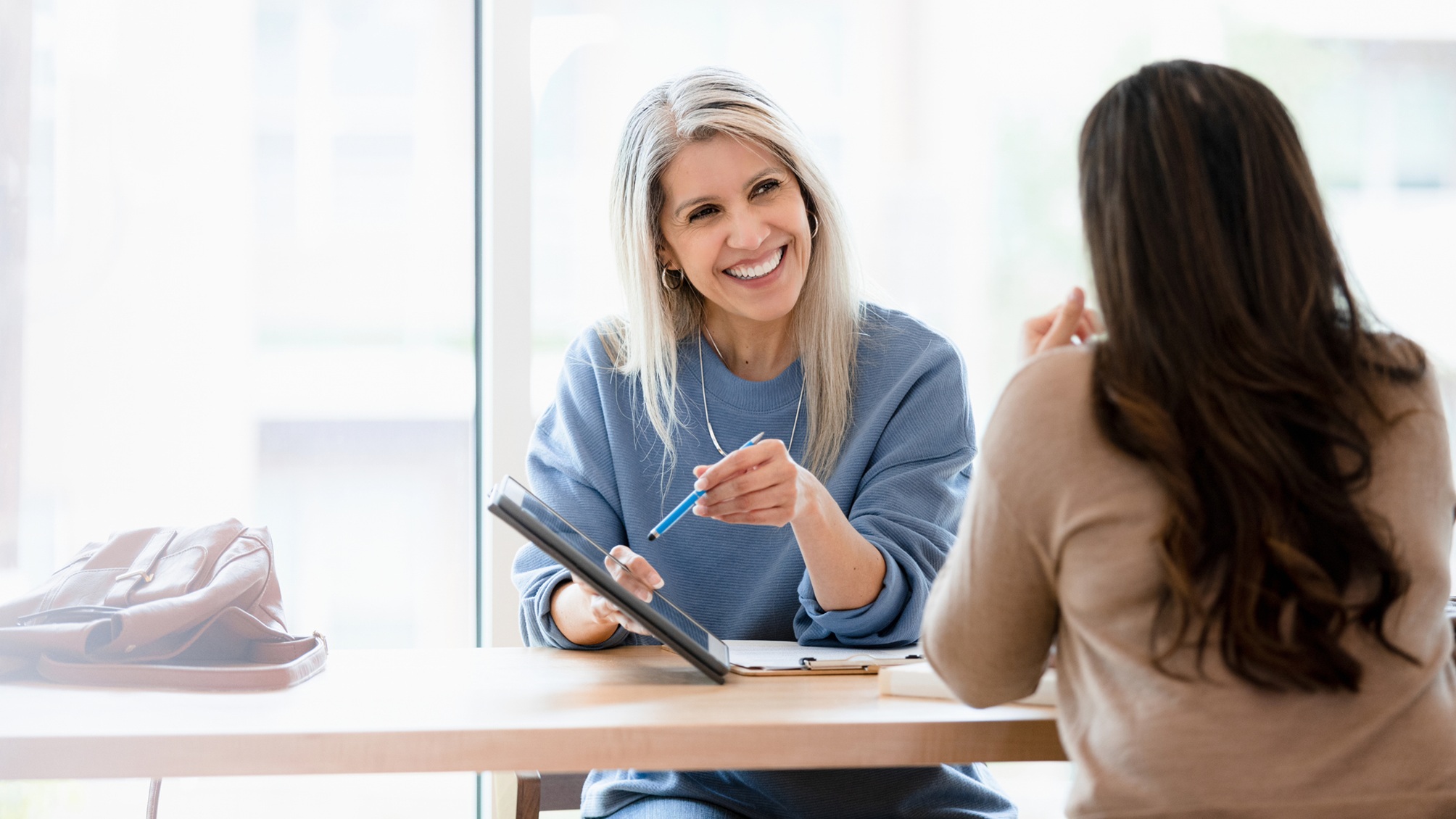 A financial adviser smiles as she shows a tablet to a female client.