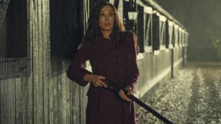 Locked In still image showing Famke Janssen looking scared holding a rifle