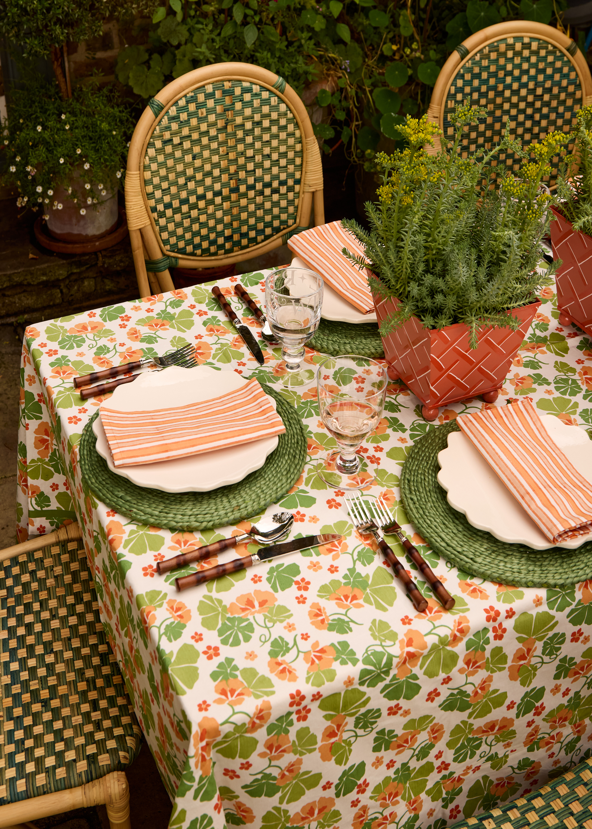 An outdoor table laid for dinner with a floral tablecloth and green placemats