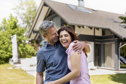 A happy, middle-aged couple in front of their home.