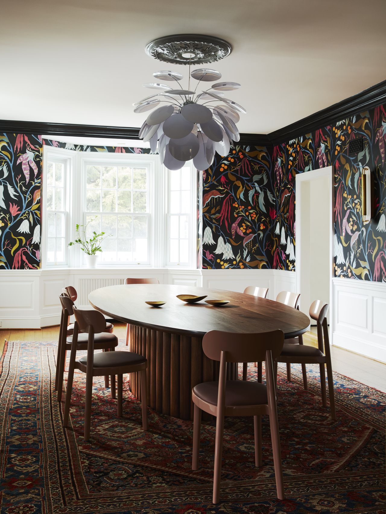 A dining room with dark-toned wallpaper, a dining table and a chandelier on top